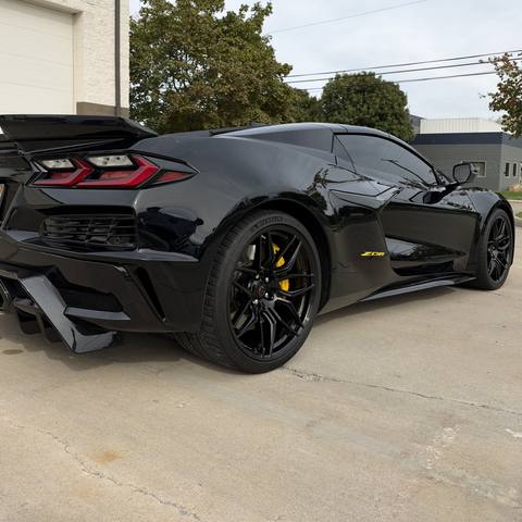 Rear three quarter view of a black mid-engine Corvette with yellow brake calipers