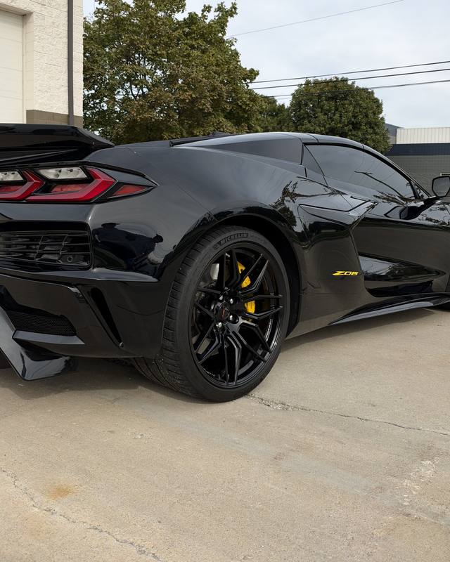 Rear three quarter view of a black mid-engine Corvette with yellow brake calipers