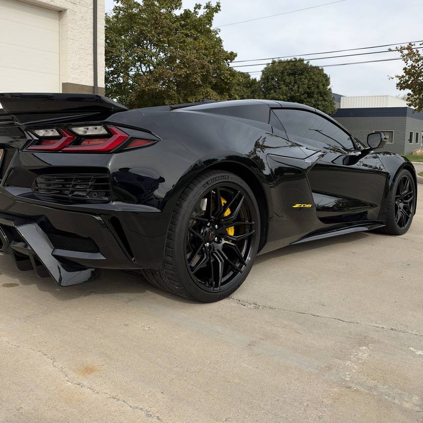 Rear three quarter view of a black mid-engine Corvette with yellow brake calipers