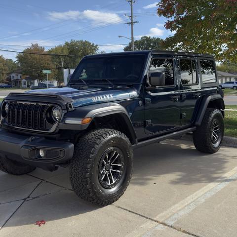 Black four door Jeep on all terrain tires under a blue sky