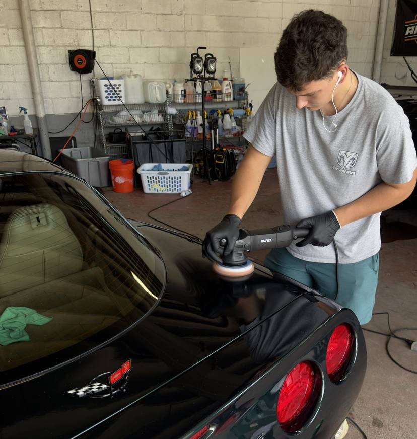 A Refresh My Ride technician machine polishing the rear of a black Corvette inside the shop