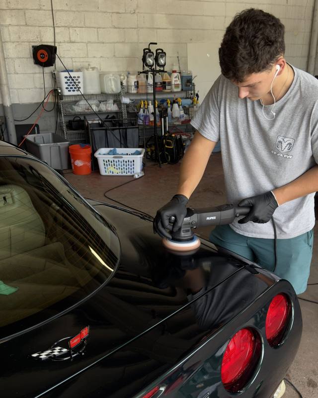 A Refresh My Ride technician machine polishing the rear of a black Corvette inside the shop