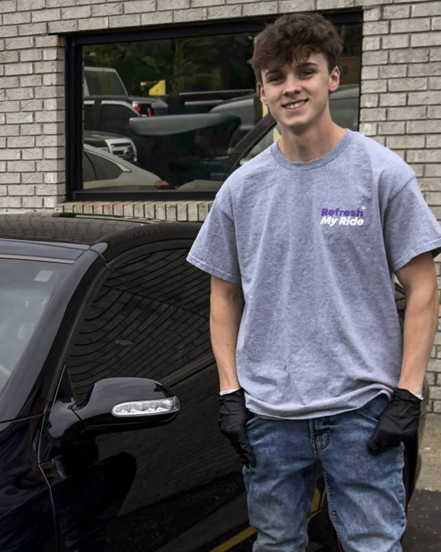 Josh Meller, owner of Refresh My Ride, standing beside a black coupe outside the shop