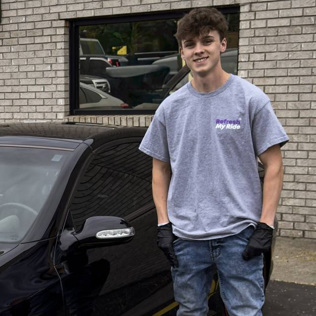Josh Meller, owner of Refresh My Ride, standing beside a black coupe outside the shop