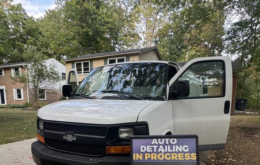 The white Refresh My Ride mobile detailing van at a customer’s home, beside a sign reading Auto detailing in progress