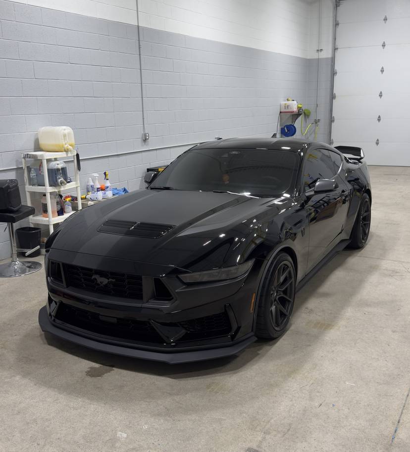 Black Ford Mustang parked in a bright white bay inside the shop