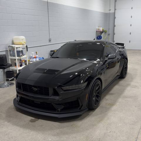 Black Ford Mustang parked in a bright white bay inside the shop