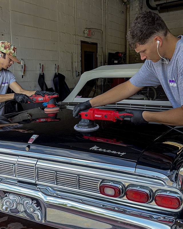 Two Refresh My Ride technicians machine polishing the trunk of a classic black Mercury