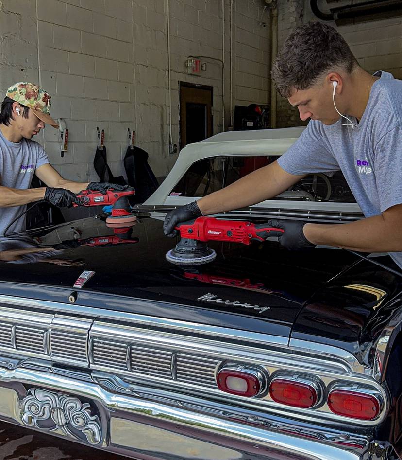 Two Refresh My Ride technicians machine polishing the trunk of a classic black Mercury
