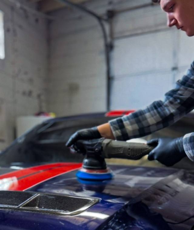 Technician machine polishing the striped hood of a Mustang
